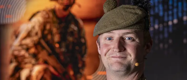 Soldier Stood in camouflage uniform and beret posing for a portrait in front of an Army Expo Poster