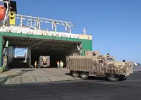 A brown armoured vehicle is pictured driving off of a ship and onto a port. 