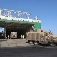 A brown armoured vehicle is pictured driving off of a ship and onto a port.
