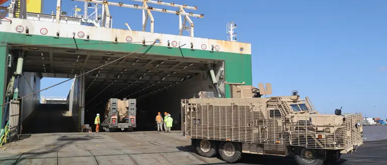 A brown armoured vehicle is pictured driving off of a ship and onto a port.