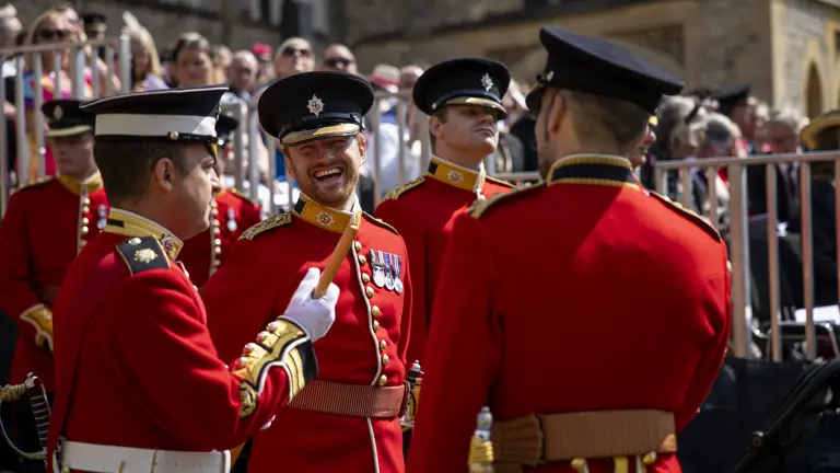 An Army officer laughs during a conversation with a soldier, they are both wearing red tunics.