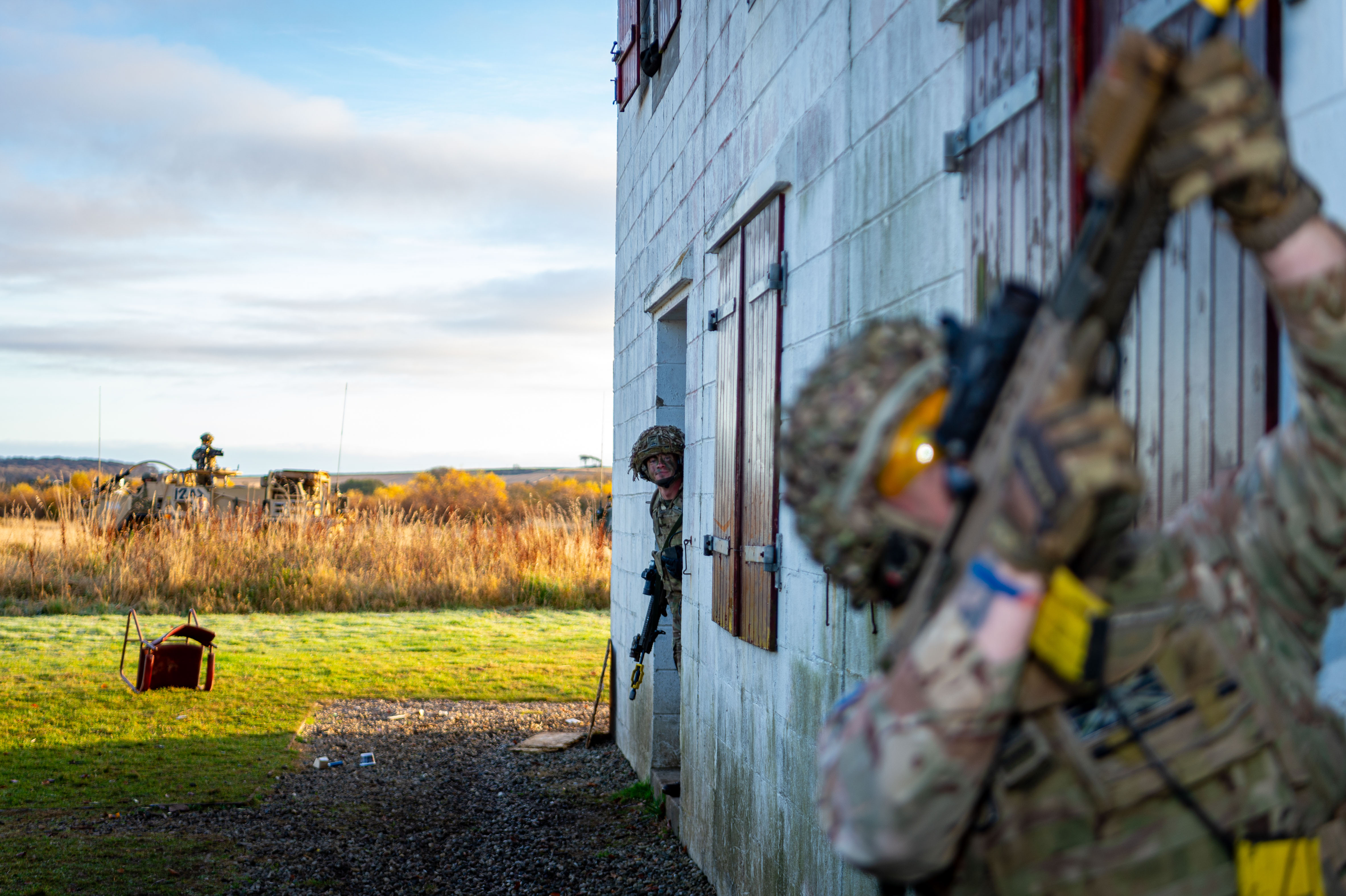 Two personnel in uniform are pictured outside of a makeshift house during an urban training drill. 
