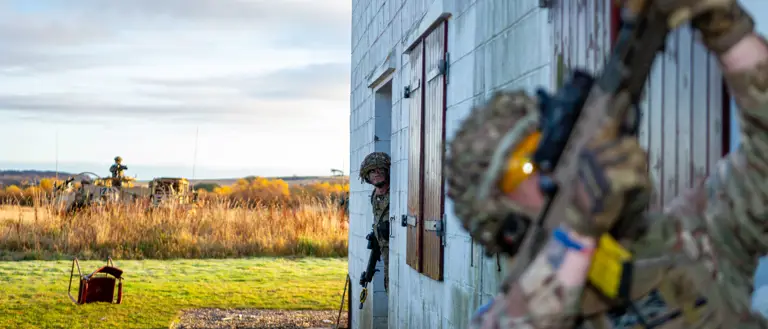 Two personnel in uniform are pictured outside of a makeshift house during an urban training drill.