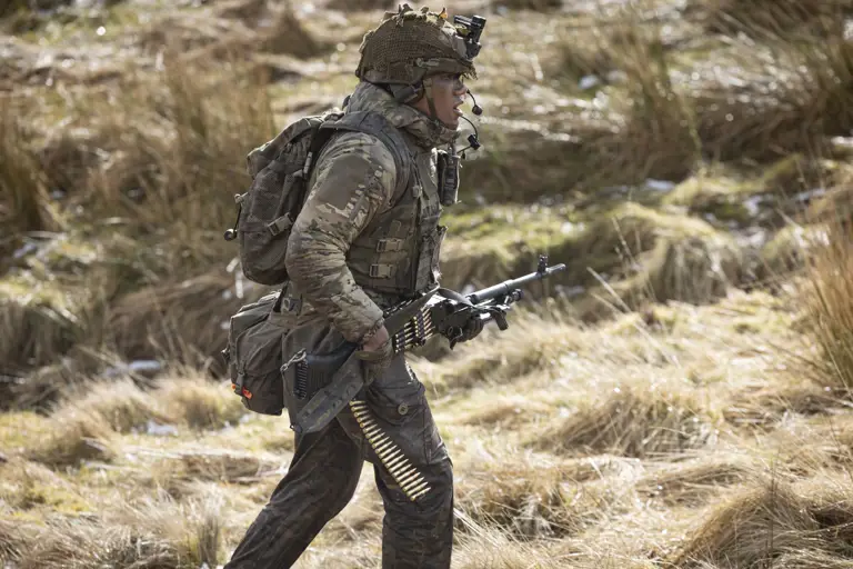 Soldier in camouflage uniform wearing body armour and helmet walks in the firing range holding his weapon