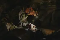 Soldier wearing camouflage and helmet with a headlamp providing medical aid in a dimly lit environment.