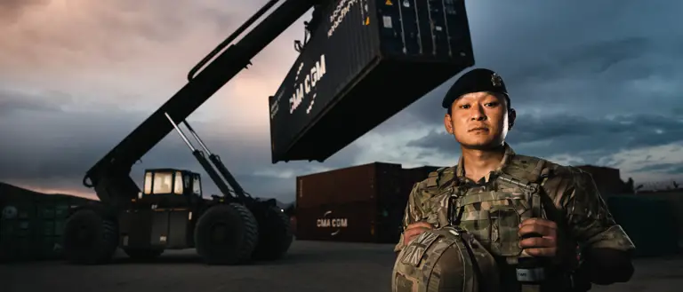 Lance Corporal (LCpl) Bishal Rai stands in front of the Rough Terrain Container Handler (RTCH)