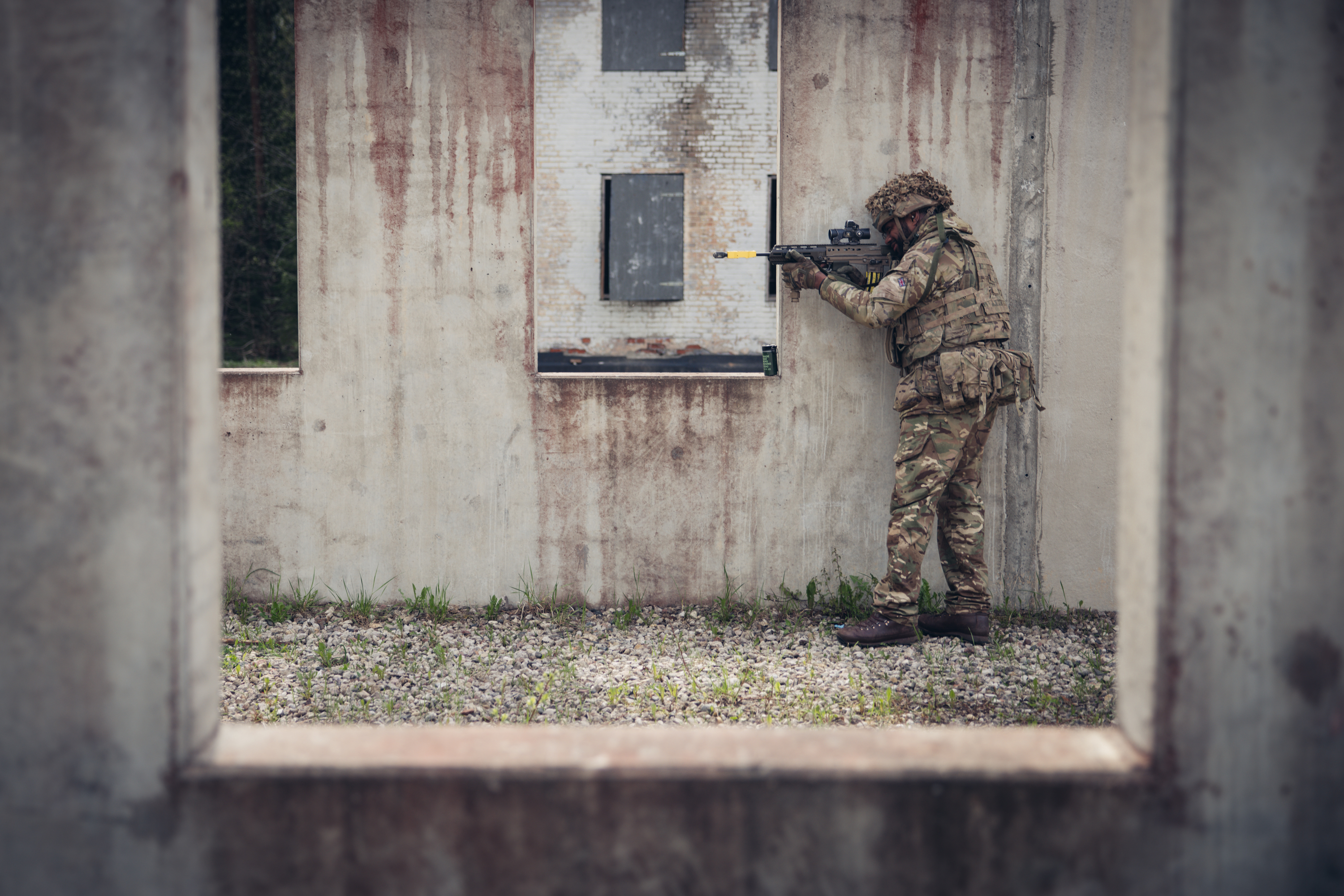 A soldier wearing camouflage uniform holds a rifle up to a window.