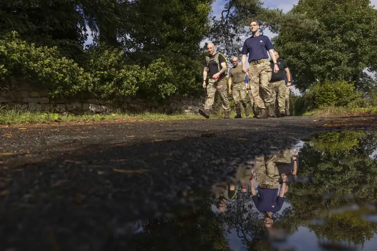 Six soldiers wearing camouflage trousers and a jumper, walking outside