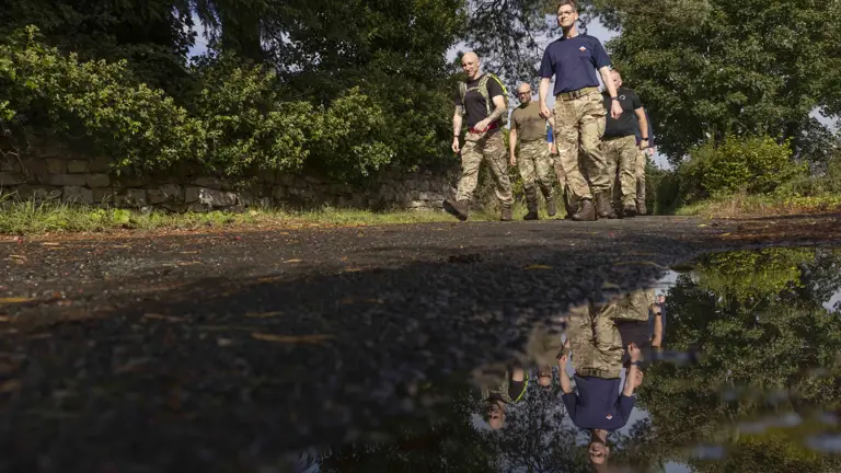 Six soldiers wearing camouflage trousers and a jumper, walking outside