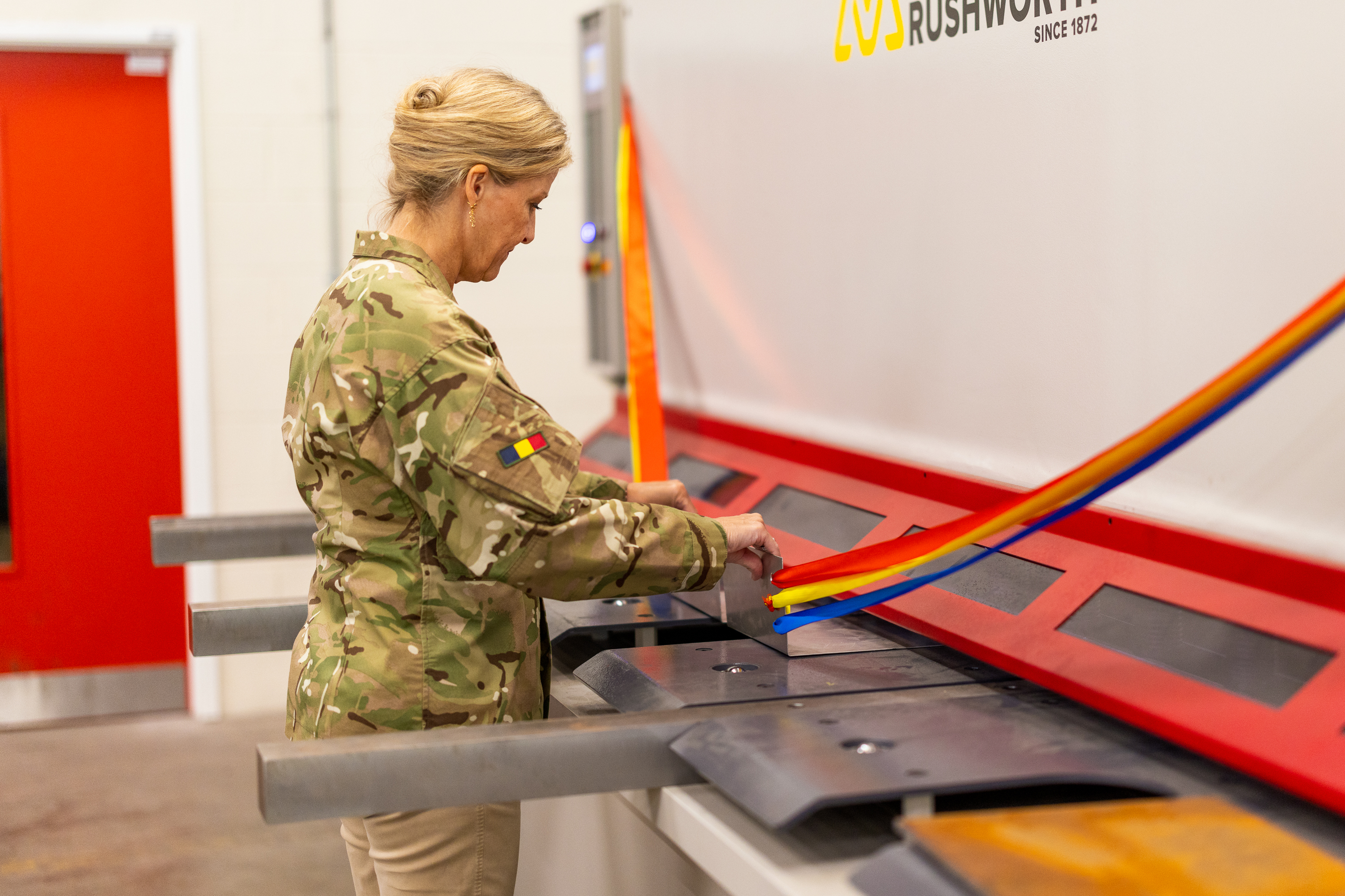 The Duchess of Edinburgh is seen wearing trousers and a camouflage print jacket stood testing out some equipment. 