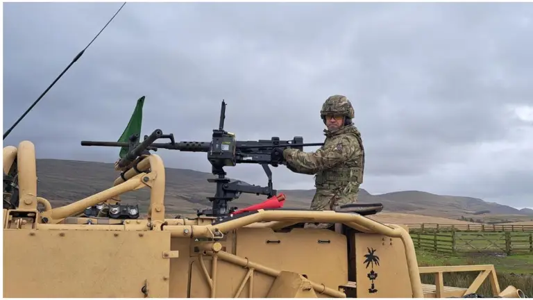 A man in uniform is pictured on top of a military vehicle manning a weapon. 