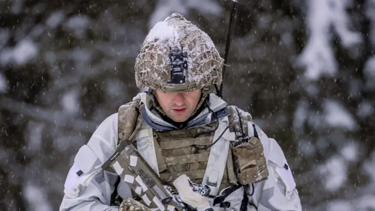 A soldier in white camo traverses snowy terrain with his rifle.