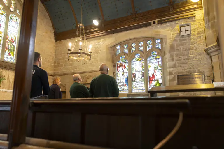 Six soldiers wearing camouflage trousers and a jumper, stand in a church for a talk before their walk.