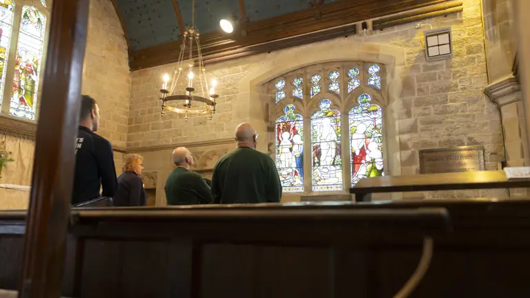 Six soldiers wearing camouflage trousers and a jumper, stand in a church for a talk before their walk.