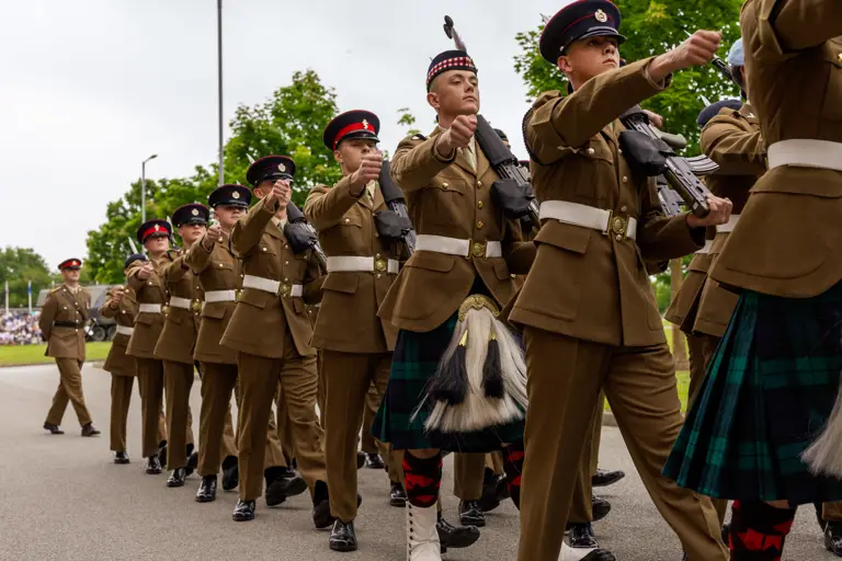 A row of soldiers in their brown uniform holding a rifle are seen marching in time with each other on parade.