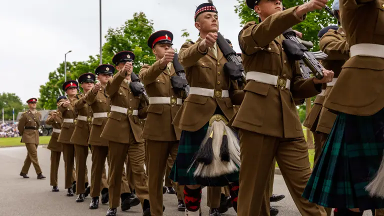 A row of soldiers in their brown uniform holding a rifle are seen marching in time with each other on parade.