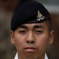 A British Gurkha soldier is facing the camera, wearing a dark blue beret on his head, featuring the King's Gurkha Artillery cap badge.