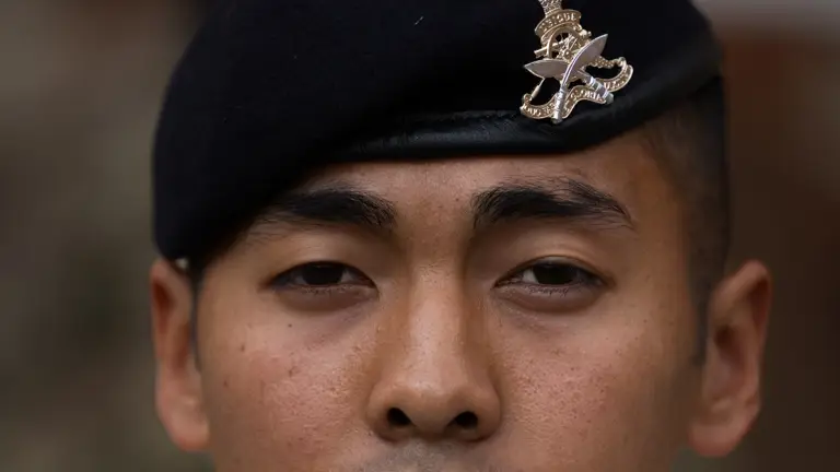 A British Gurkha soldier is facing the camera, wearing a dark blue beret on his head, featuring the King's Gurkha Artillery cap badge.