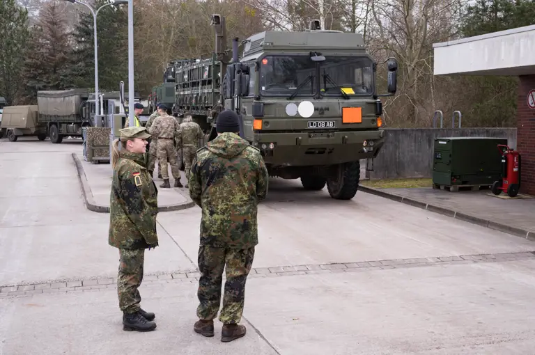 Two german soldiers in uniform are seen overlooking the UK soldiers also in uniform refuelling their vehicles on the German military base.