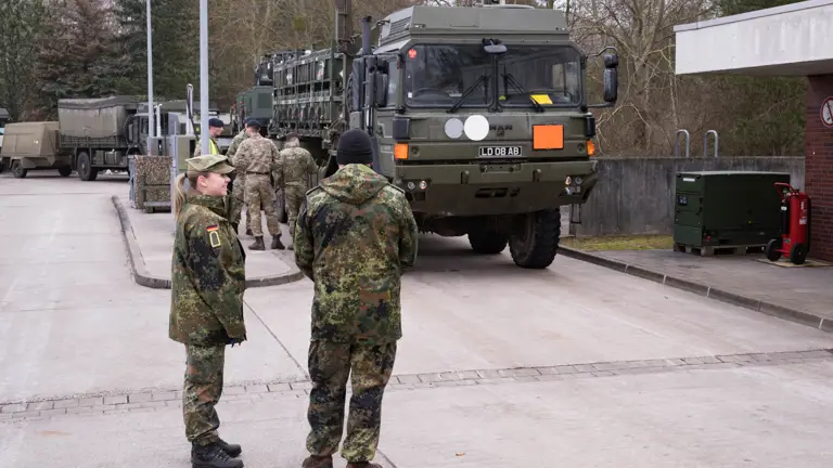 Two german soldiers in uniform are seen overlooking the UK soldiers also in uniform refuelling their vehicles on the German military base.