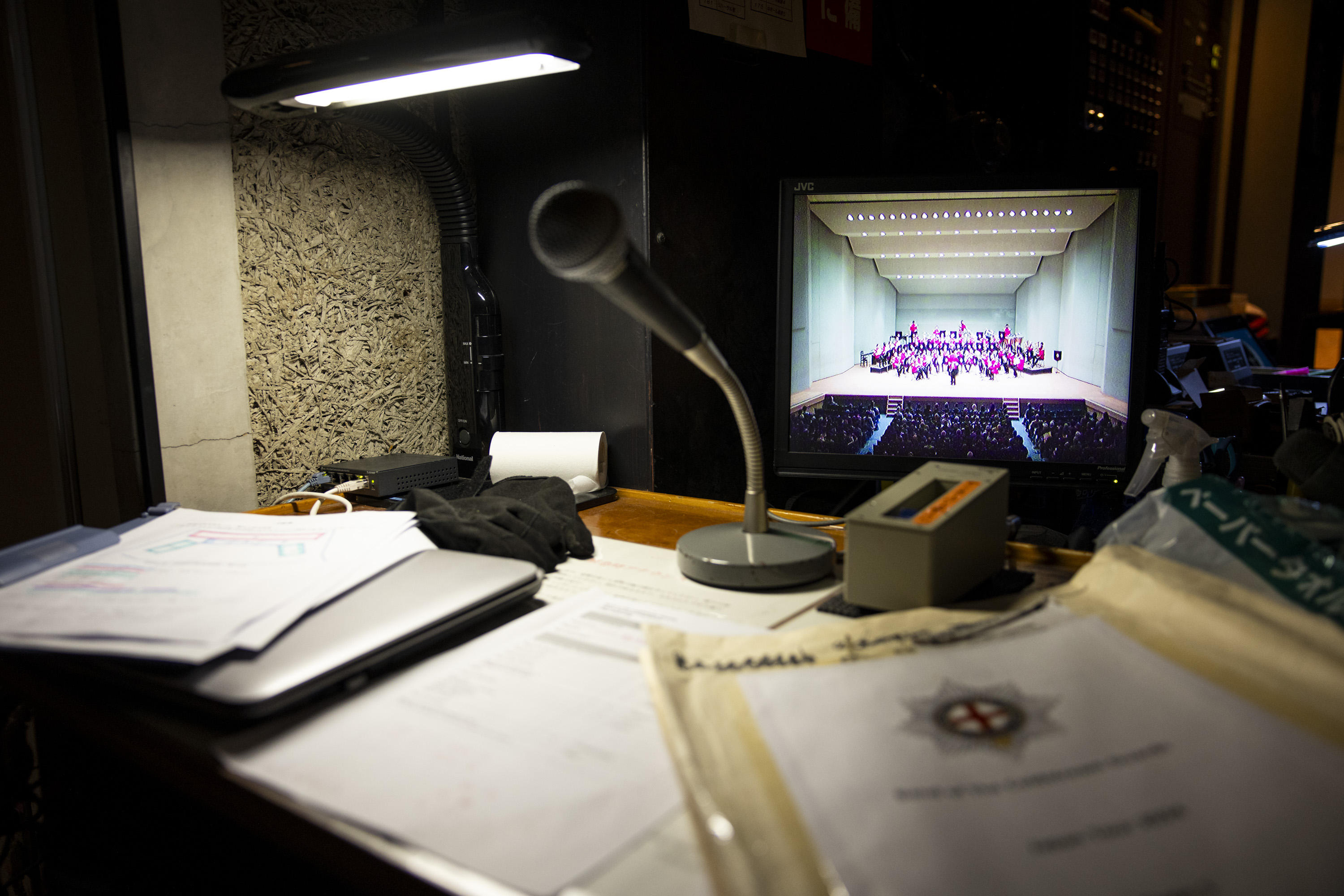 A behind the scenes shot of a concert hall, there is a television showing a livestream of the concert. 