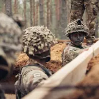 Three soldiers wearing camouflague uniforms stand in a trench. They are reinforcing the sides of the trench with wooden planks.