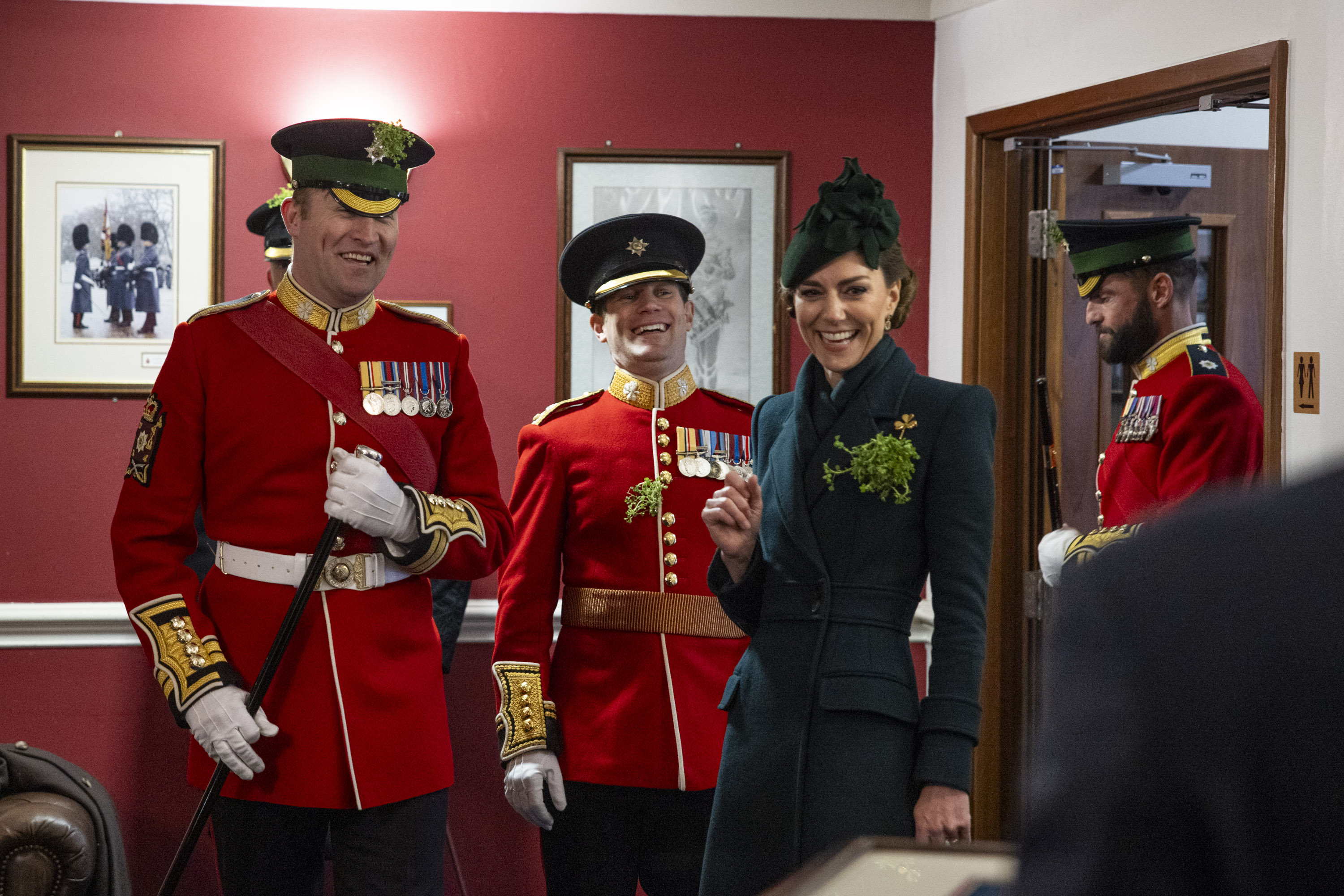 Her Royal Highness The Princess of Wales smiles in the company of personnel wearing red tunics and shamrocks. 