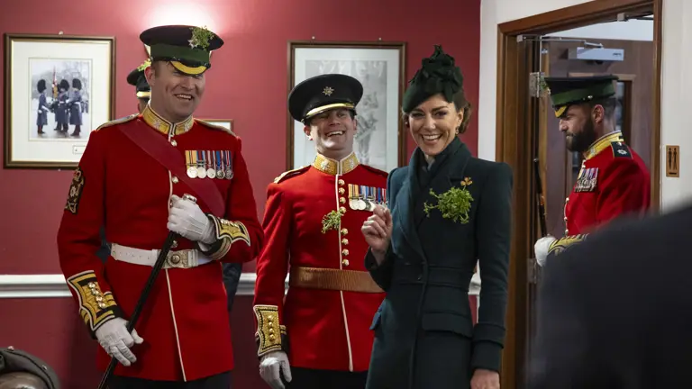 Her Royal Highness The Princess of Wales smiles in the company of personnel wearing red tunics and shamrocks.