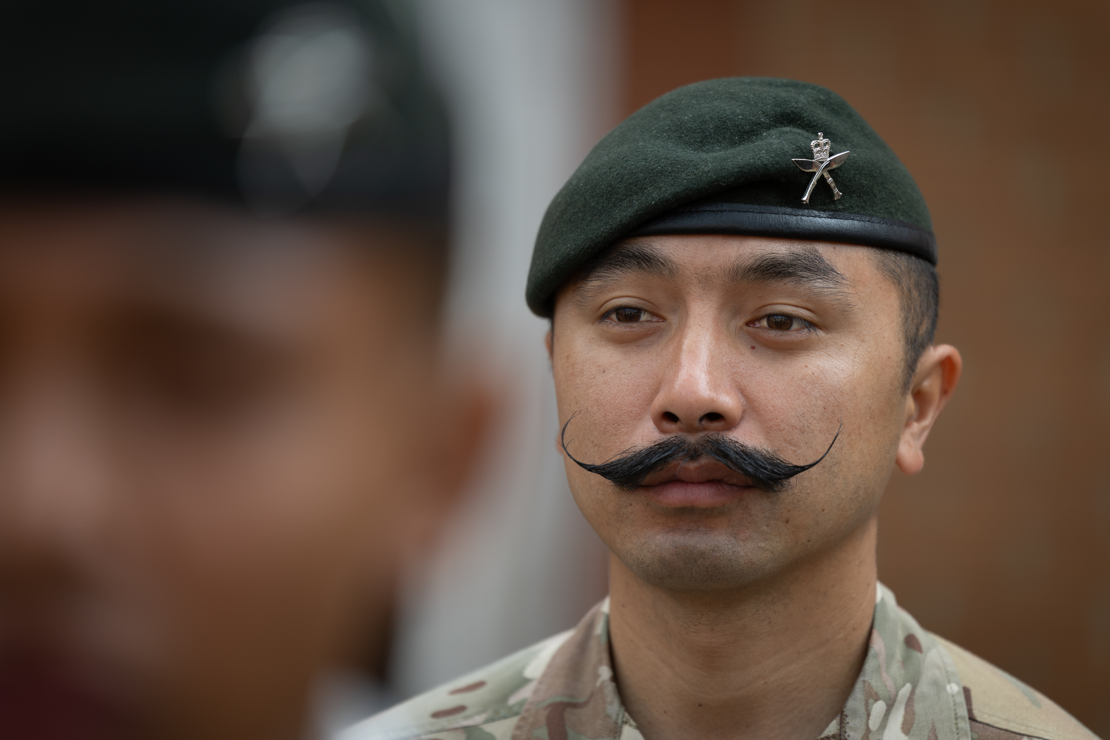 Military personnel wearing camouflaged uniform and a green beret with a distinctive emblem are focused. 