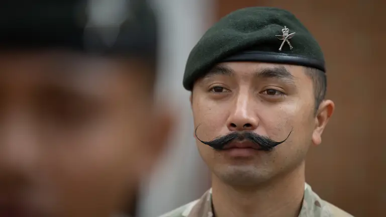 Military personnel wearing camouflaged uniform and a green beret with a distinctive emblem are focused.