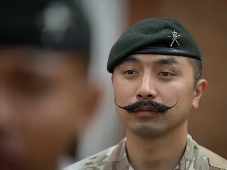 Military personnel wearing camouflaged uniform and a green beret with a distinctive emblem are focused.