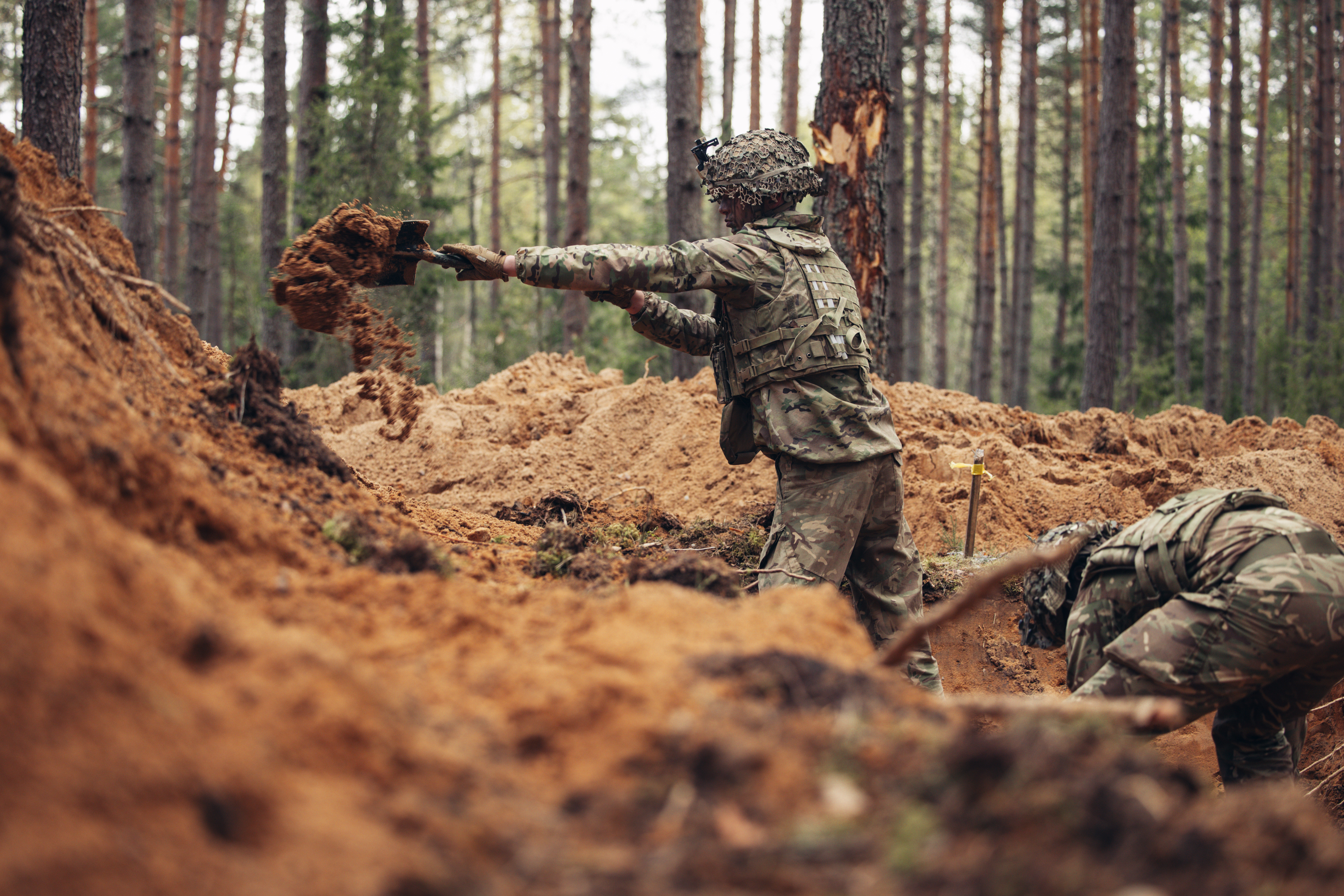 Two soldiers use shovels to dig trenches.