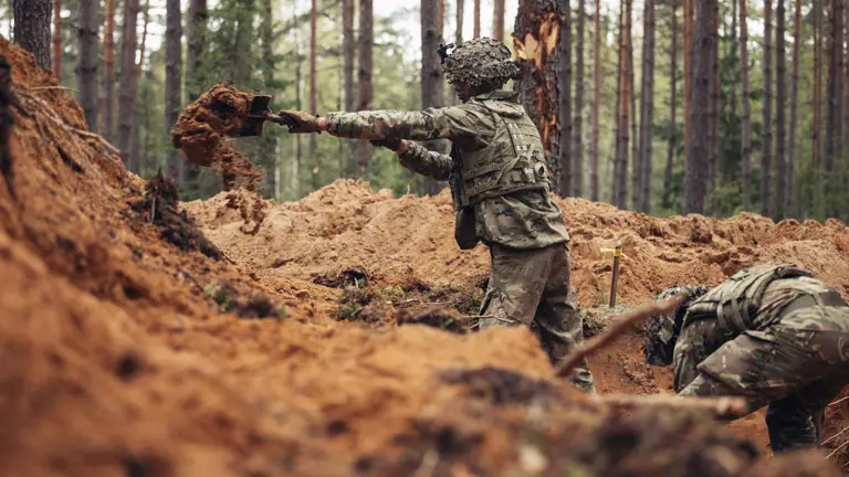 Two soldiers use shovels to dig trenches.