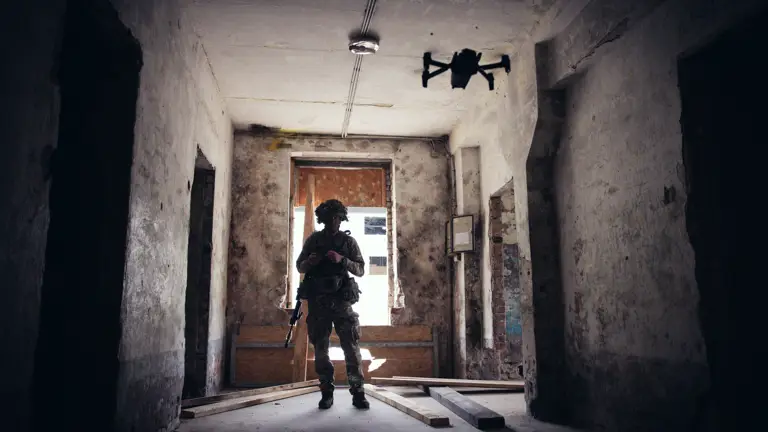A soldier in uniform operates a drone inside of a building.