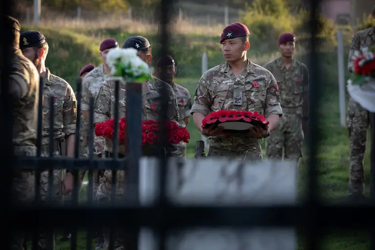 A soldier wearing camouflage uniform and a maroon beret holds a poppy wreath.