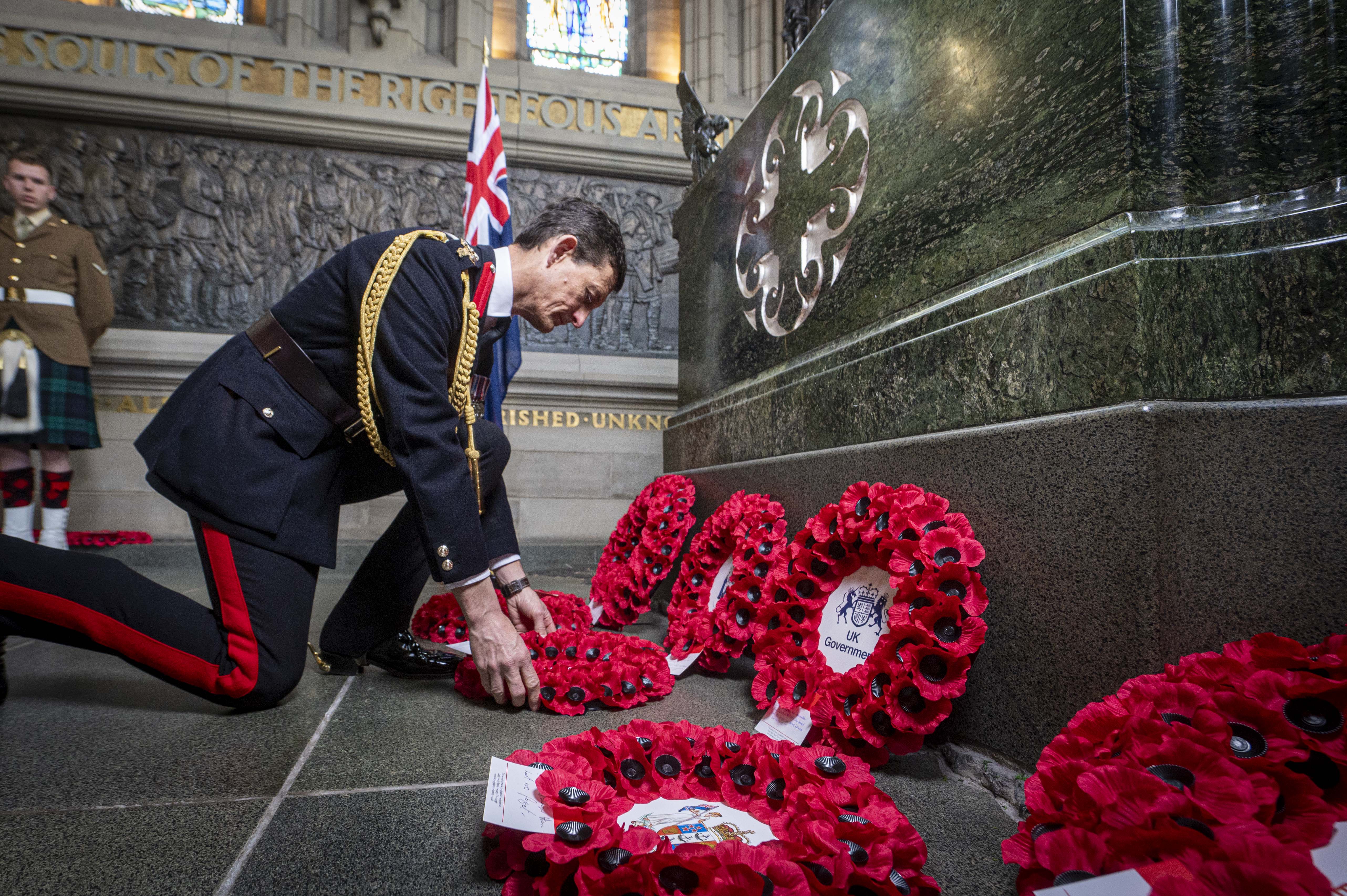 A man in a black ceremonial military uniform lays a wreath.