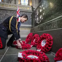 A man in a black ceremonial military uniform lays a wreath.