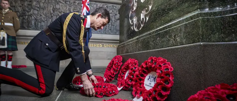 A man in a black ceremonial military uniform lays a wreath.