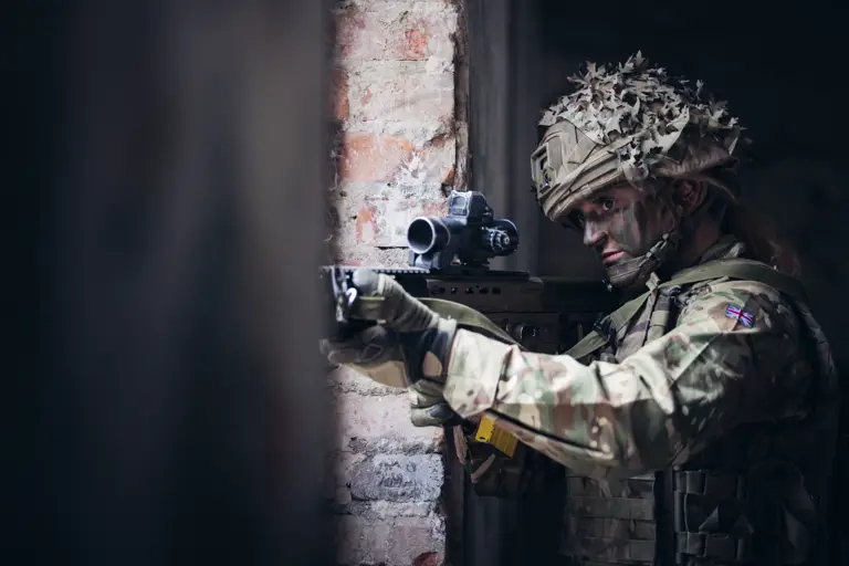A female soldier takes aim with her rifle through a window.