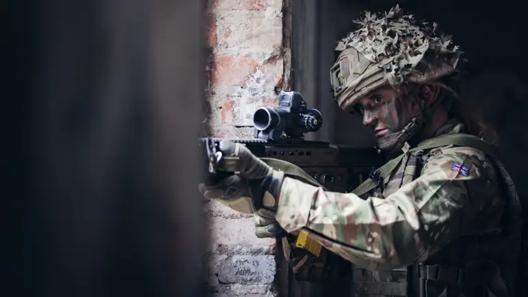 A female soldier takes aim with her rifle through a window.