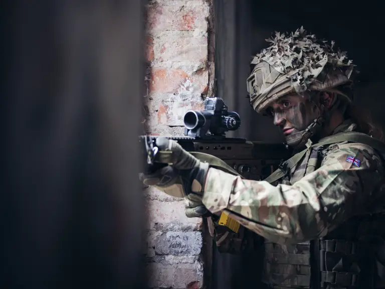 A female soldier takes aim with her rifle through a window.