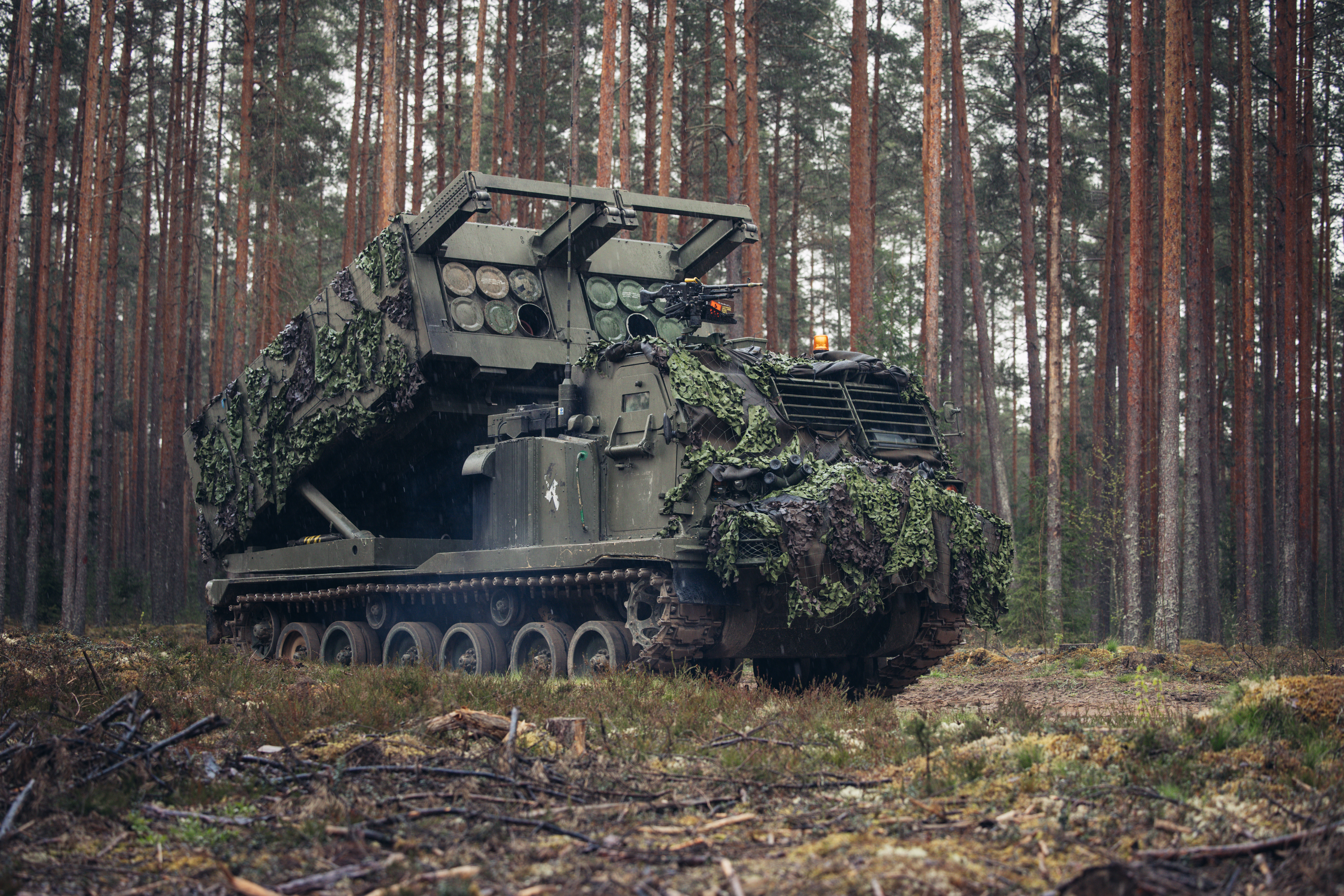 A camouflaged military tracked vehicle, specifically an M270 Multiple Launch Rocket System (MLRS).
