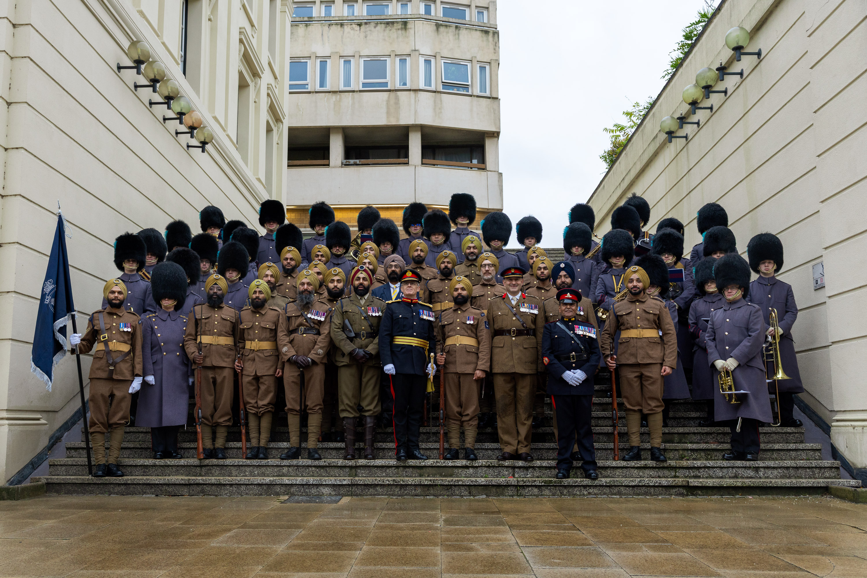 Group portrait of British soldiers and officers in ceremonial uniforms, including bearskin hats, standing on outdoor steps.