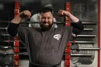 A person in a gym confidently flexes their muscles, wearing a t-shirt with the