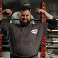 A person in a gym confidently flexes their muscles, wearing a t-shirt with the