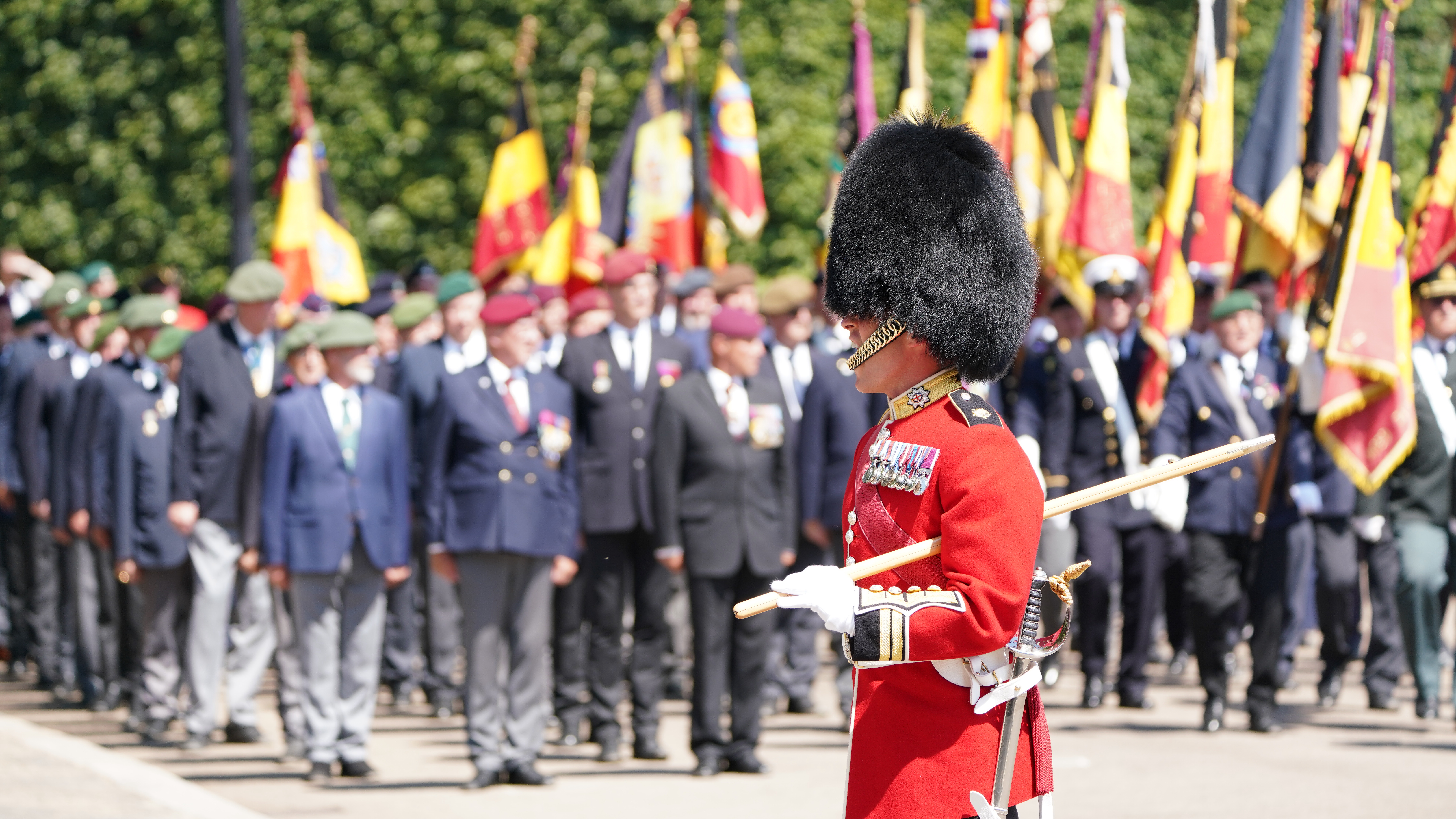 A person in a red ceremonial uniform and bearskin hat stands in the foreground. 