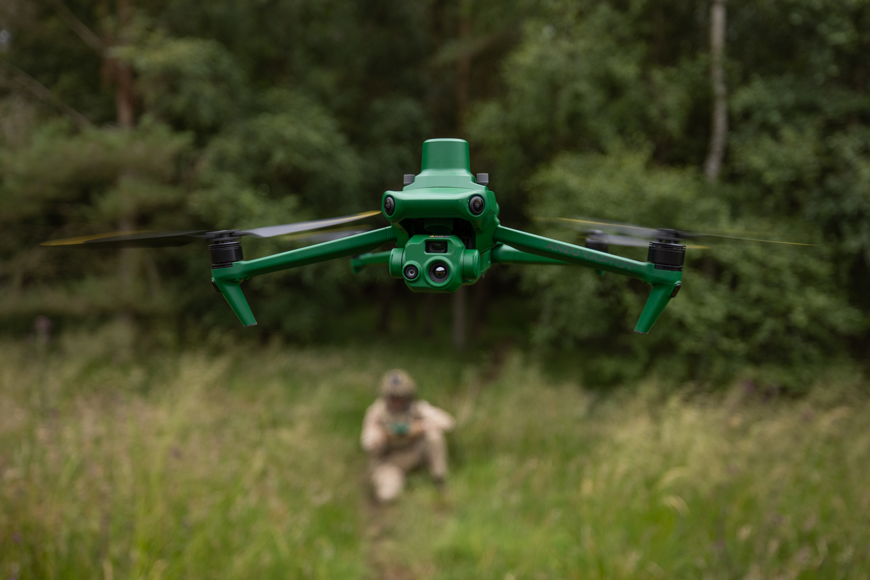 A green aerial drone with multiple sensors flying over a grassy area.