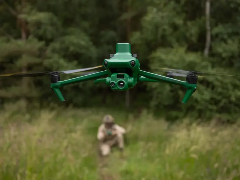 A green aerial drone with multiple sensors flying over a grassy area.