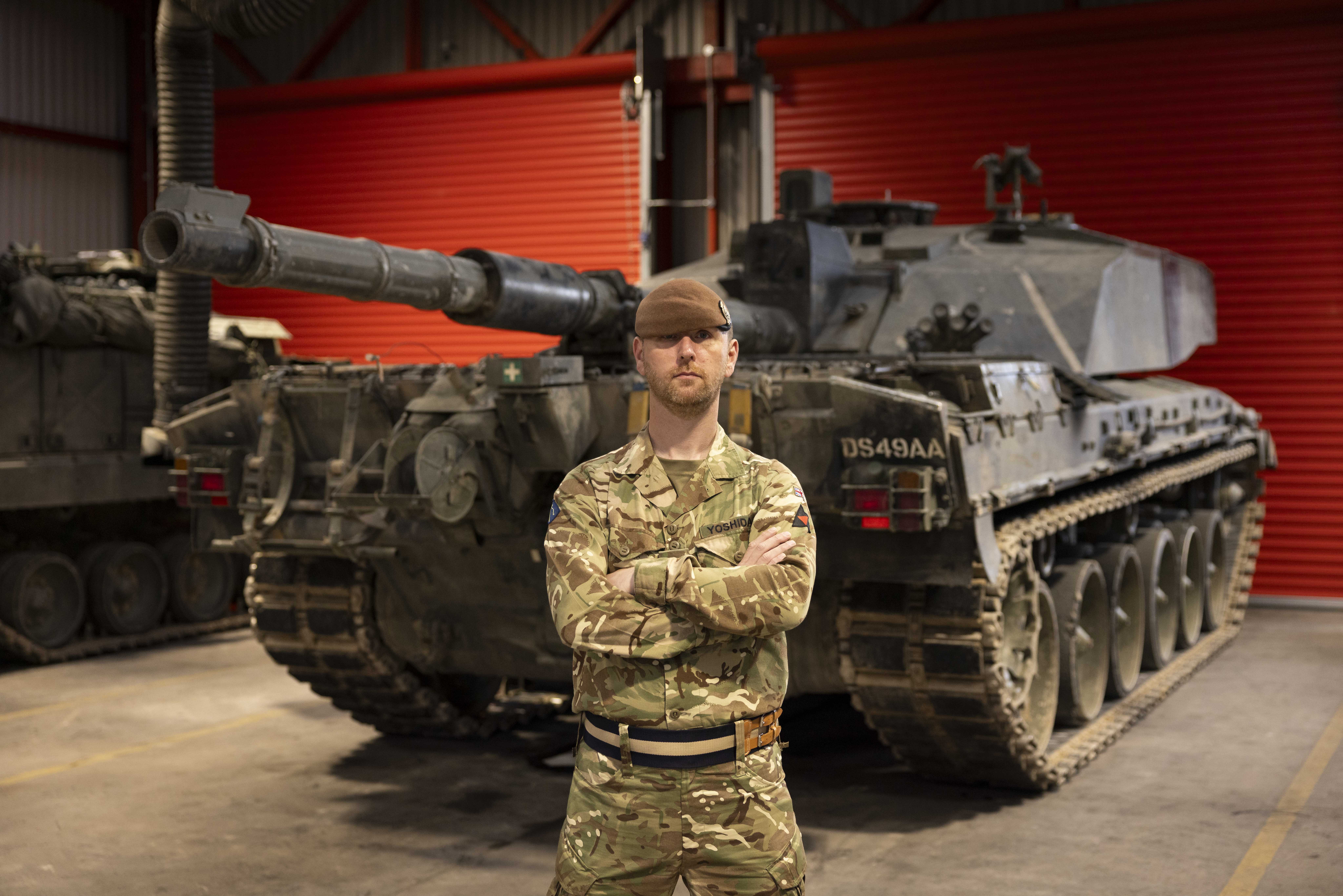 A man in uniform stands with his arms crossed in front of a tank. 