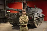 A man in uniform stands with his arms crossed in front of a tank. 